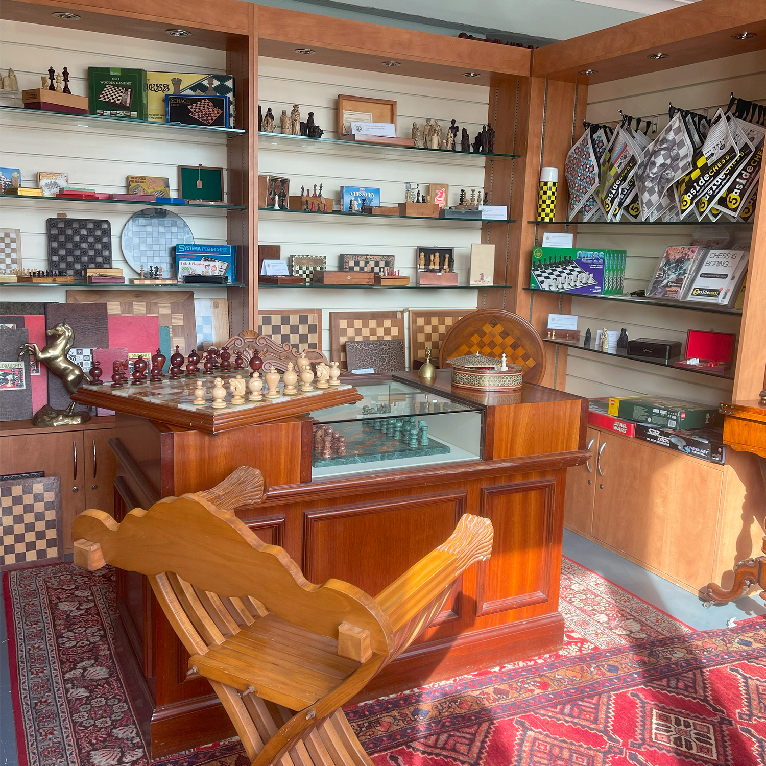 Wooden chessboard with chess pieces and a chair in a store setting with shelves of products.