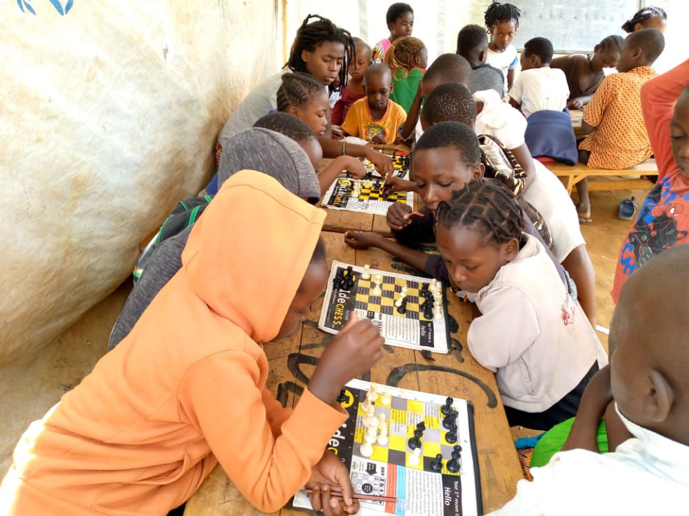Children playing 5asideCHESS at a table with other children in the background.